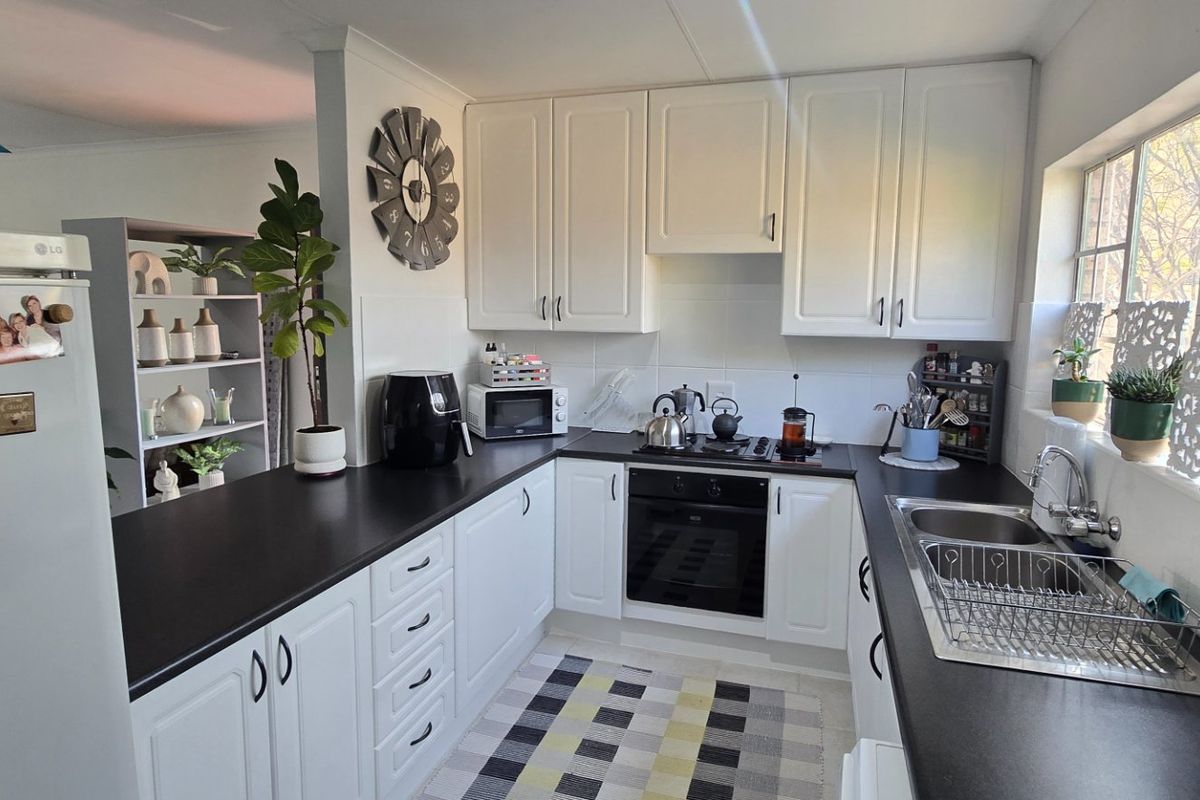 A functional kitchen featuring white cabinetry, dark countertops, a built-in oven, gas hob, and a stainless steel sink with natural light.