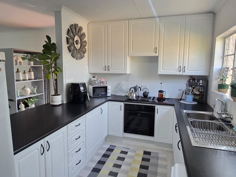 A functional kitchen featuring white cabinetry, dark countertops, a built-in oven, gas hob, and a stainless steel sink with natural light.