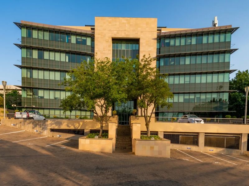 Modern multi-story commercial office building featuring a glass curtain wall facade, stone cladding, and integrated paved parking facilities.