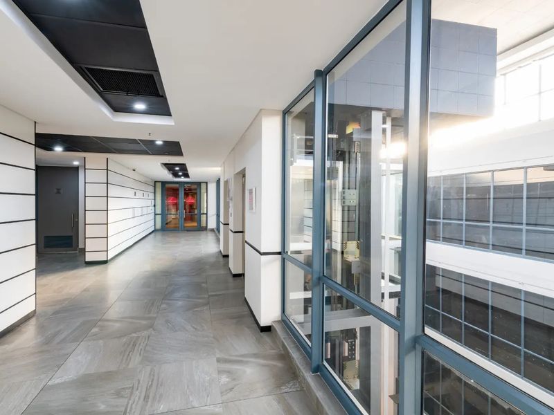 Modern commercial hallway featuring tiled flooring, recessed ceiling lighting, and a prominent glass-enclosed elevator shaft.