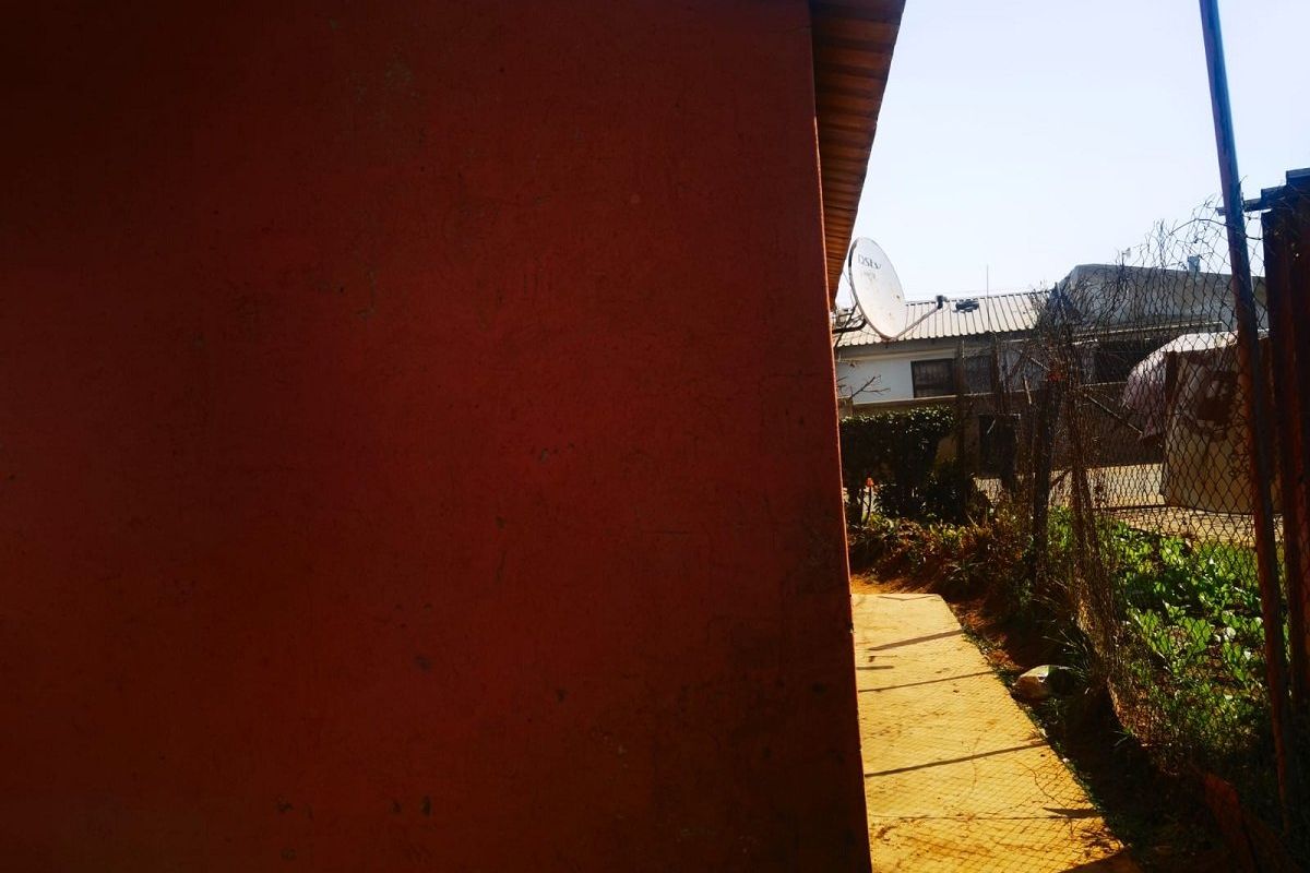 A view of the rear exterior area showing a side wall, a concrete pathway, and perimeter chain link fencing.