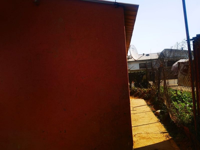 A view of the rear exterior area showing a side wall, a concrete pathway, and perimeter chain link fencing.