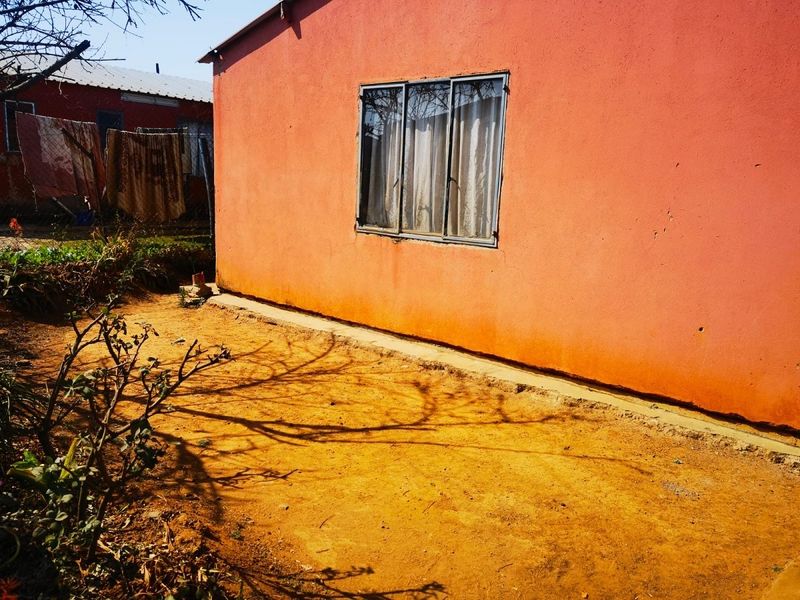 Rear exterior view of the property featuring a painted facade, sliding window, and an unpaved garden area.