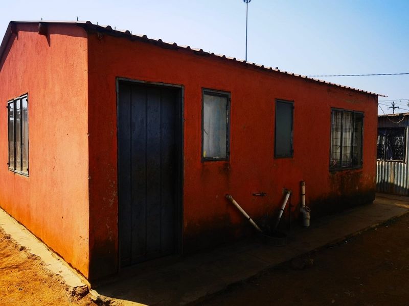 Exterior view of a single-story structure featuring a metal roof, painted masonry walls, and exposed exterior plumbing fixtures.