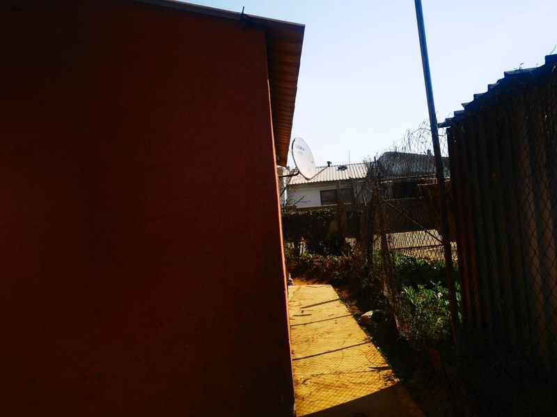 A narrow side passage between the house exterior and a chain-link boundary fence, featuring a concrete path and mounted satellite dish.
