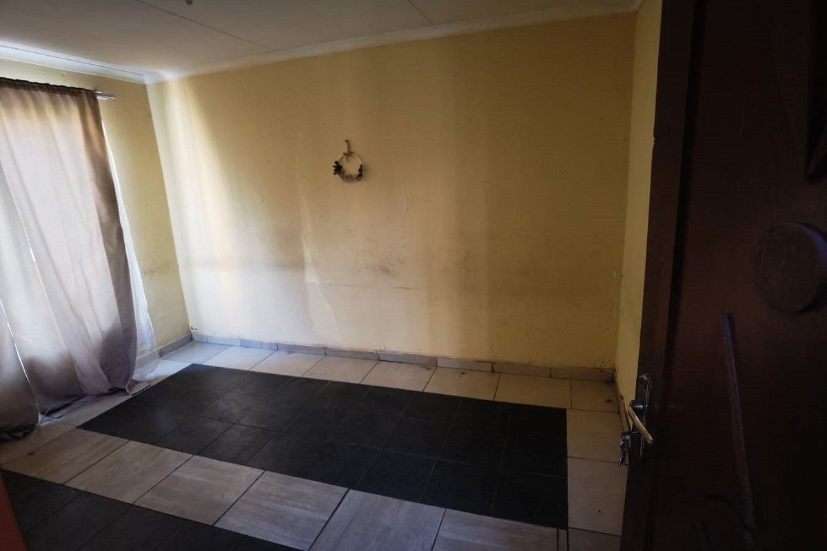 An empty bedroom featuring two-tone tiled flooring and plain walls, offering a blank canvas for renovation or interior design updates.