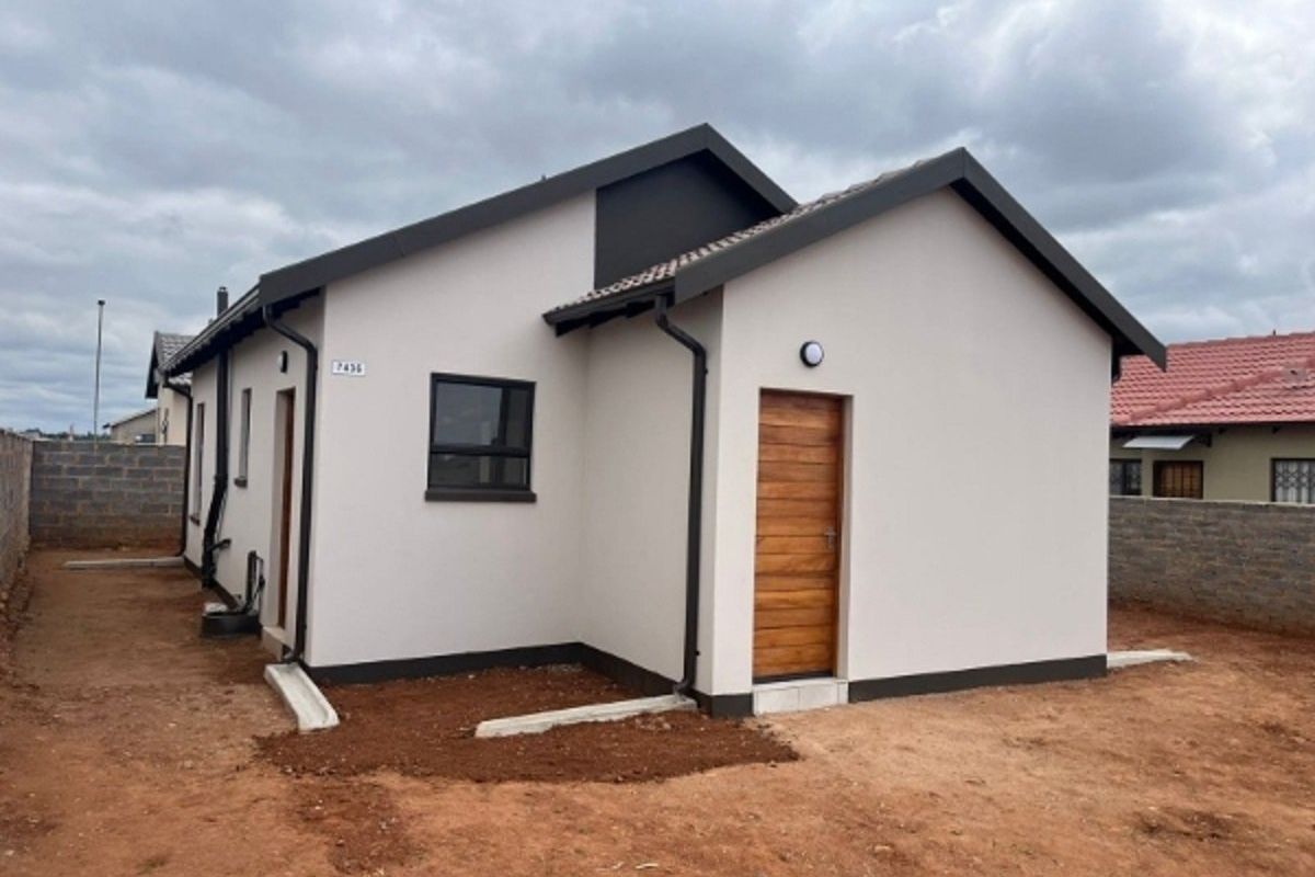 A modern single-story house exterior featuring a tiled roof, neutral painted walls, timber door, and aluminium window frames, set on an unlandscaped plot.