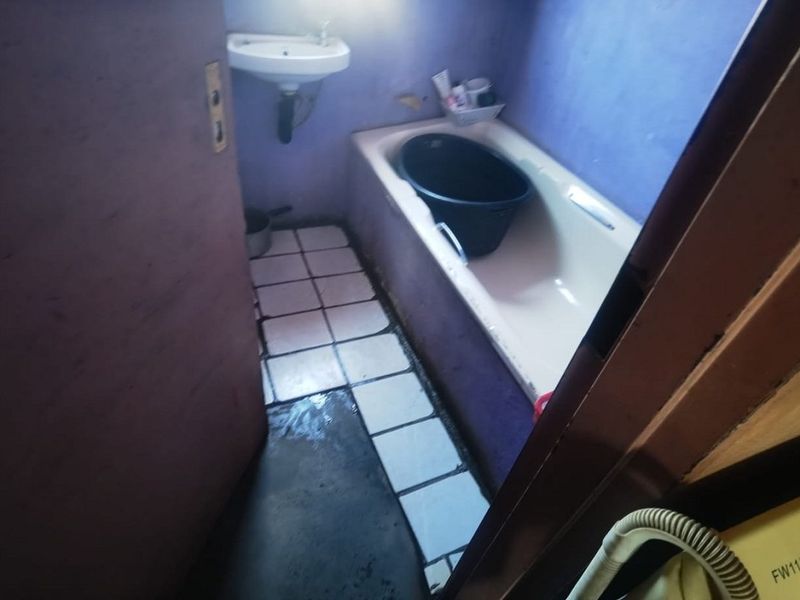 A small bathroom featuring a bathtub, wall-mounted basin, and tiled flooring, currently requiring maintenance and cosmetic updates to improve its condition.