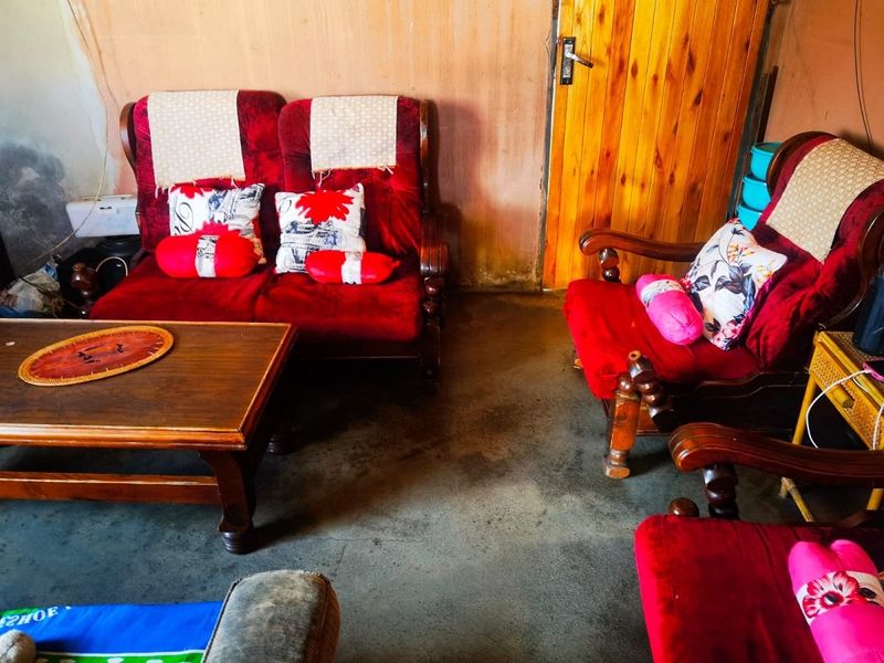 A living room area featuring a timber door and concrete flooring, currently showing significant signs of wear and requiring cosmetic updates.