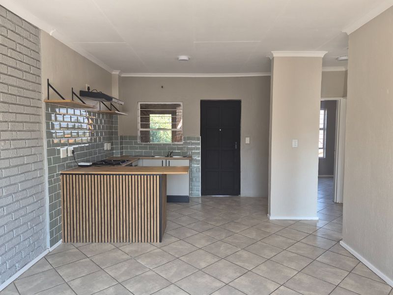 Open plan living area featuring a modern kitchen with subway tile backsplash, timber slat breakfast bar, and neutral ceramic floor tiles.