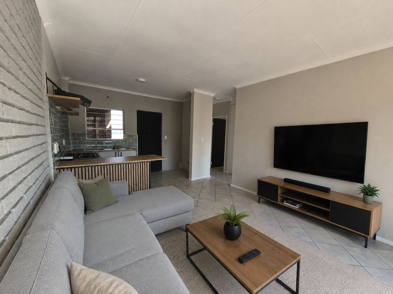 Open-plan living area featuring tiled flooring, an exposed brick feature wall, and a functional kitchen with a breakfast bar and modern cabinetry.