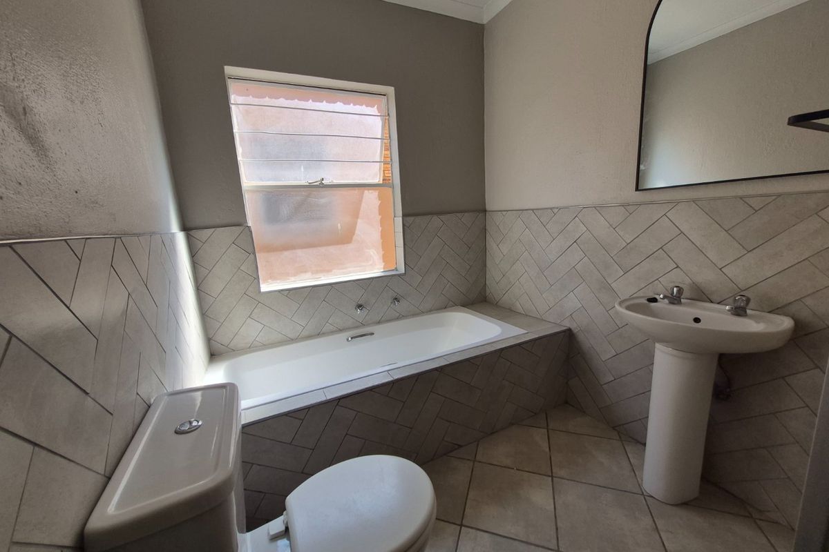 A clean, modern bathroom featuring a built-in bathtub, pedestal basin, toilet, and stylish herringbone wall tiling with neutral floor tiles.