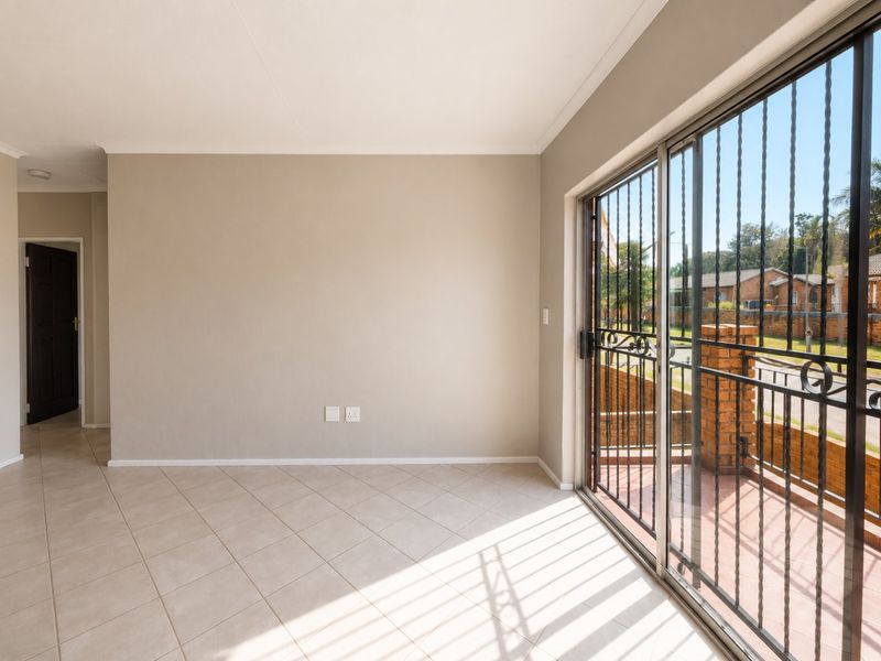 A bright, empty living area featuring neutral tiled flooring and a large sliding glass door with integrated security gate leading to an outdoor space.