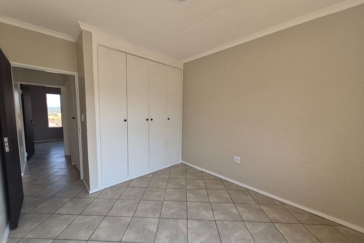 A clean, empty bedroom featuring neutral wall tones, tiled flooring, and ample built-in cupboard storage space.