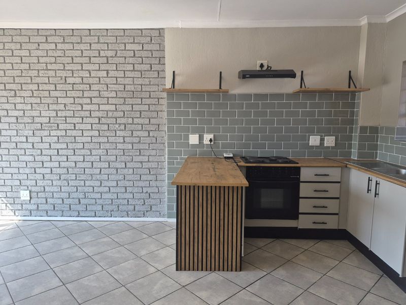 Modern kitchen featuring a subway tile backsplash, built-in oven with hob, extractor fan, floating shelves, and a stylish slatted timber island end panel.