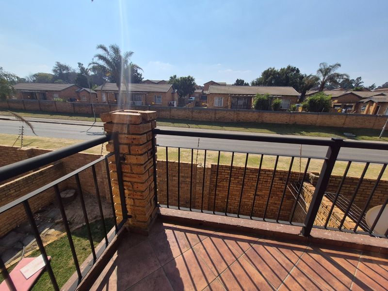 An elevated balcony featuring tiled flooring, a brick support pillar, and a metal balustrade, overlooking a residential street and neighboring properties.