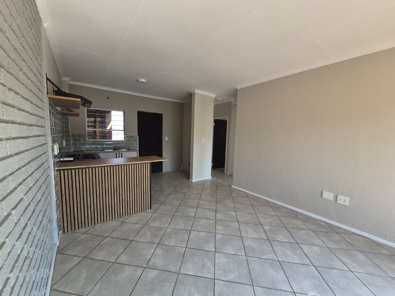 An open-plan living and kitchen area featuring tiled flooring, a modern breakfast bar, and a brick feature wall, presenting a clean and functional space.