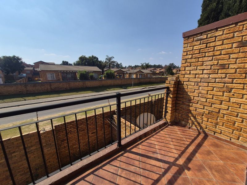 An open balcony featuring brick wall finishes, metal railings, and tiled flooring, offering an elevated view of the surrounding residential street.