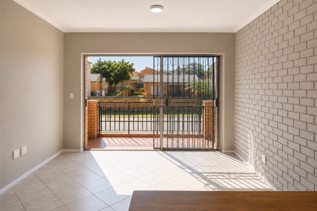 Bright and spacious living area featuring tiled floors, an exposed brick feature wall, and direct access to a private balcony through sliding glass doors.