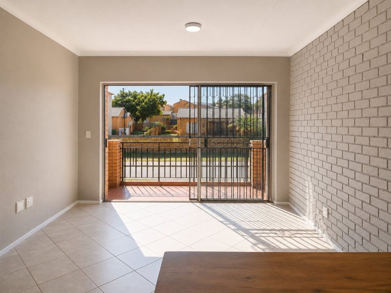 Bright and spacious living area featuring tiled floors, an exposed brick feature wall, and direct access to a private balcony through sliding glass doors.