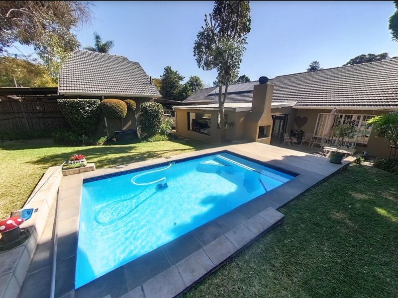 A well-maintained backyard featuring a swimming pool with tiled surround, an outdoor fireplace, and a landscaped garden area.