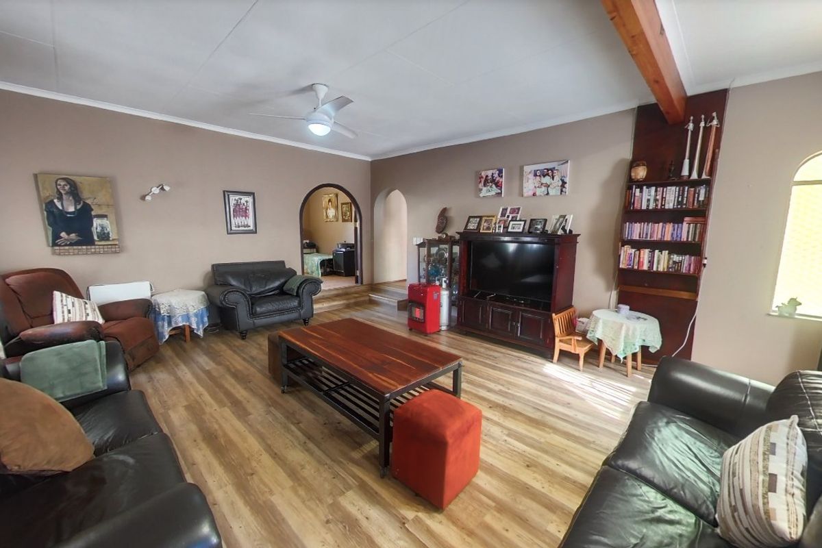 Spacious living room featuring laminate flooring, exposed timber beam, ceiling fan, and arched doorways leading to adjacent areas.