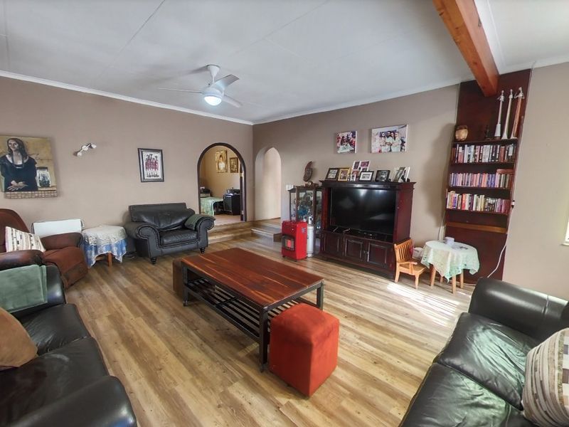 Spacious living room featuring laminate flooring, exposed timber beam, ceiling fan, and arched doorways leading to adjacent areas.