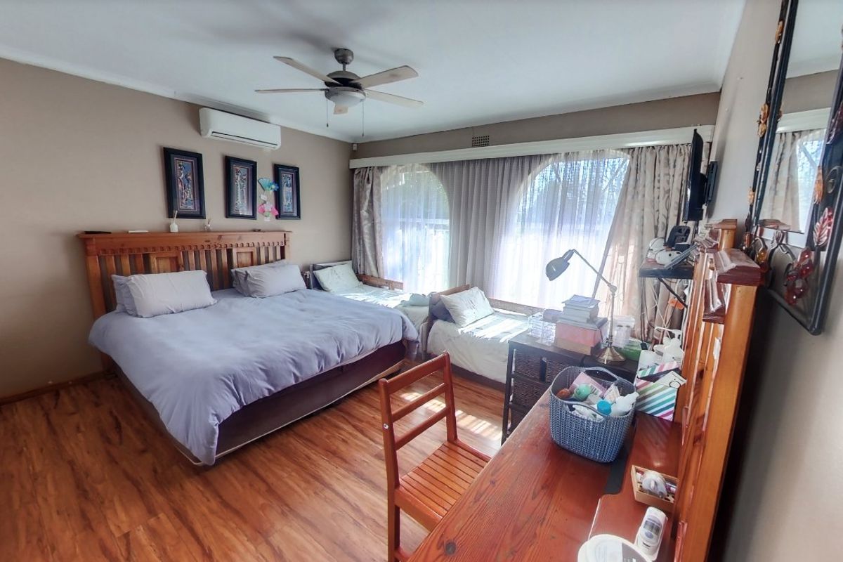 Spacious bedroom featuring laminate flooring, a ceiling fan, split-system air conditioning, and large arched windows allowing for natural light.