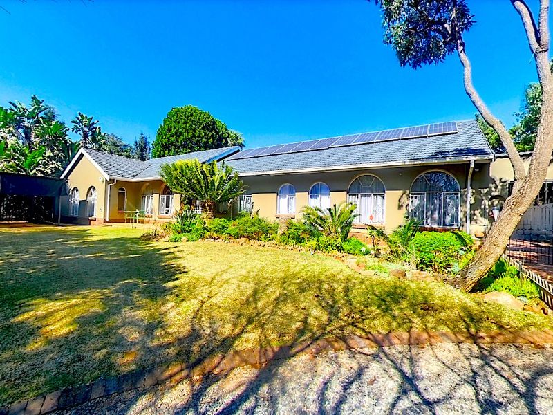 A well-maintained single-story residence featuring a tiled roof with integrated solar panels, arched windows, and a spacious front garden with a gated entrance.