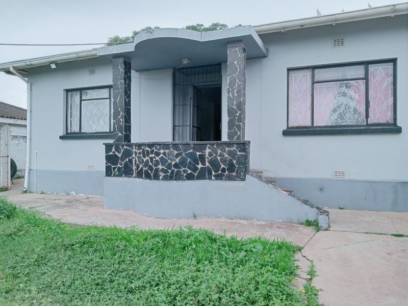 Front elevation of a single-story house featuring a stone-clad porch entrance, concrete driveway, and metal-framed windows.