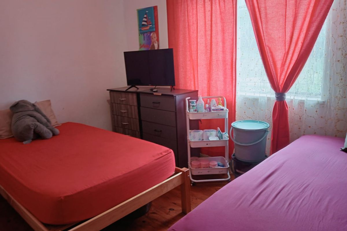 A bedroom featuring timber flooring and a window with red curtains.