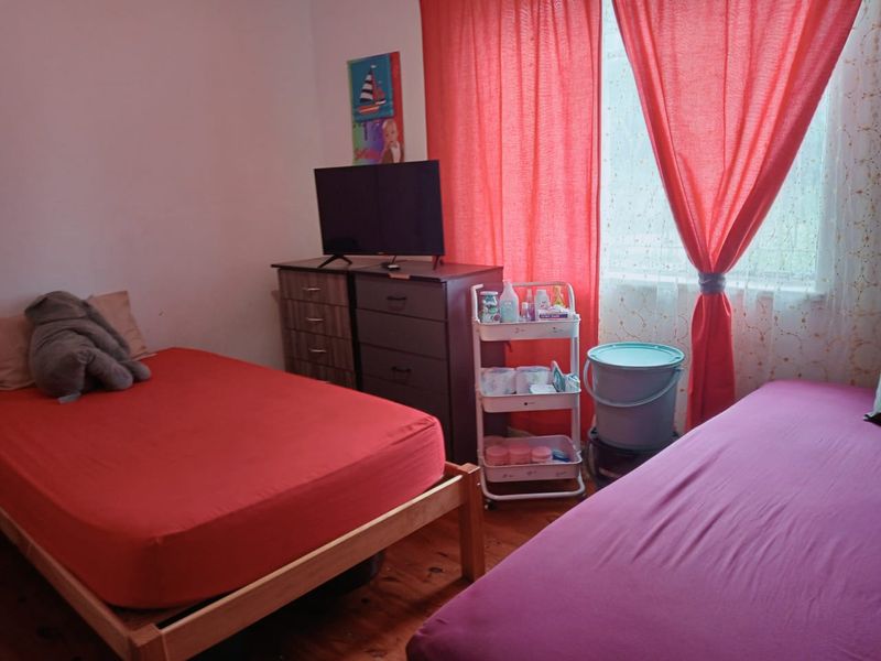 A bedroom featuring timber flooring and a window with red curtains.