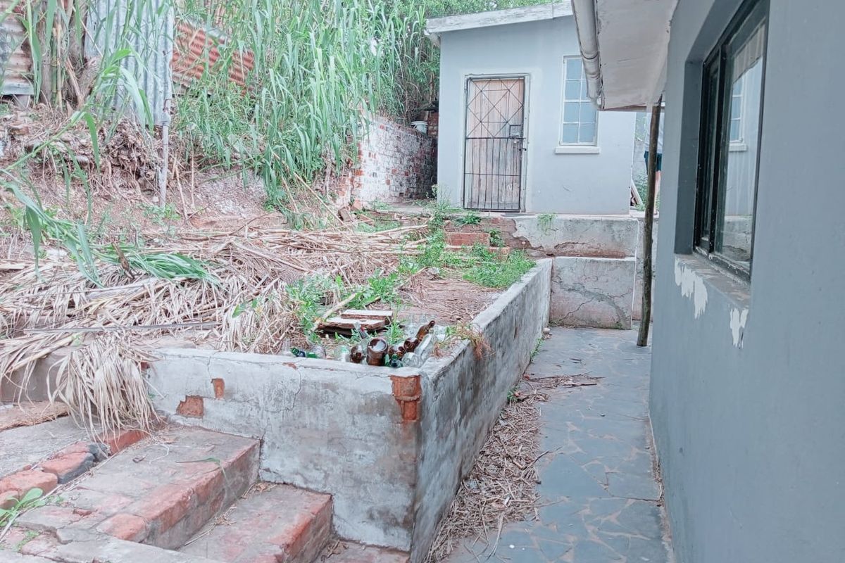 Rear exterior area featuring a paved walkway, brick retaining wall, and a small outbuilding, requiring significant landscaping and maintenance to improve the property's appeal.