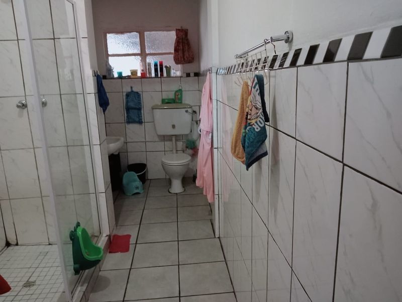 A functional bathroom featuring a shower enclosure, tiled walls and flooring, and a standard toilet suite.