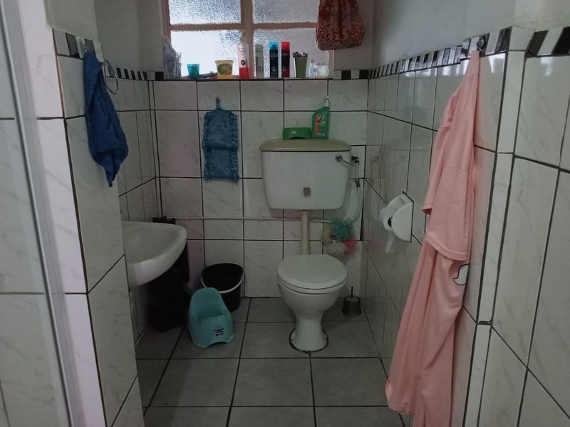 A compact bathroom featuring floor-to-ceiling ceramic tiling, a standard toilet, and a wall-mounted basin with an obscured glass window.