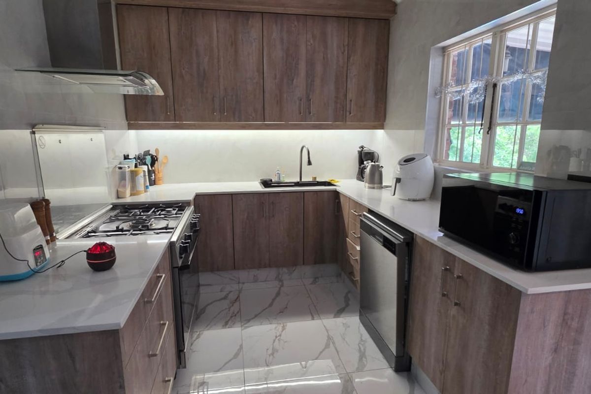 Modern kitchen featuring wood-finish cabinetry, stone countertops, gas hob, extractor fan, and marble-look floor tiles.