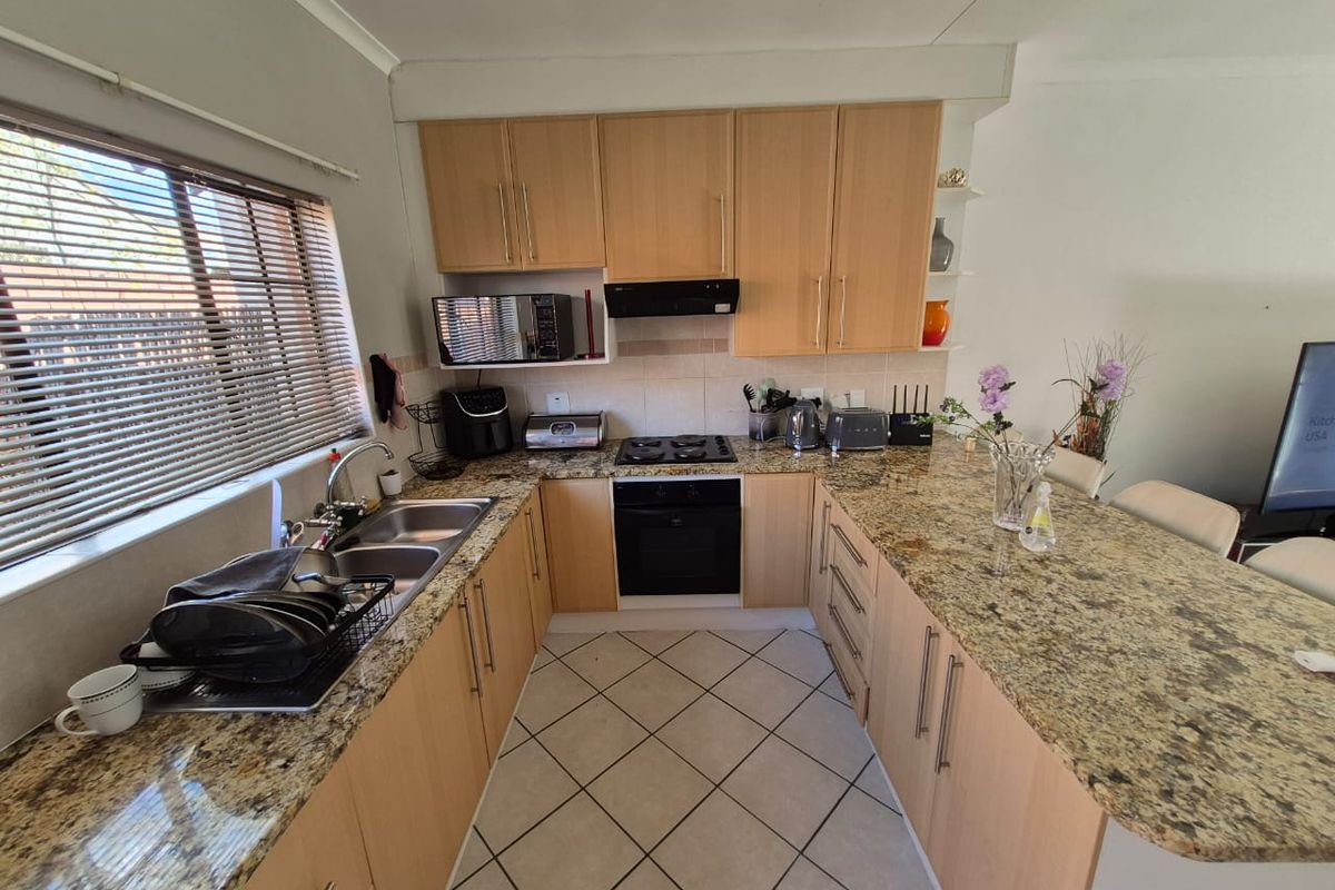A functional kitchen featuring granite countertops, light wood cabinetry, a built-in oven with gas hob, and tiled flooring with a breakfast bar area.