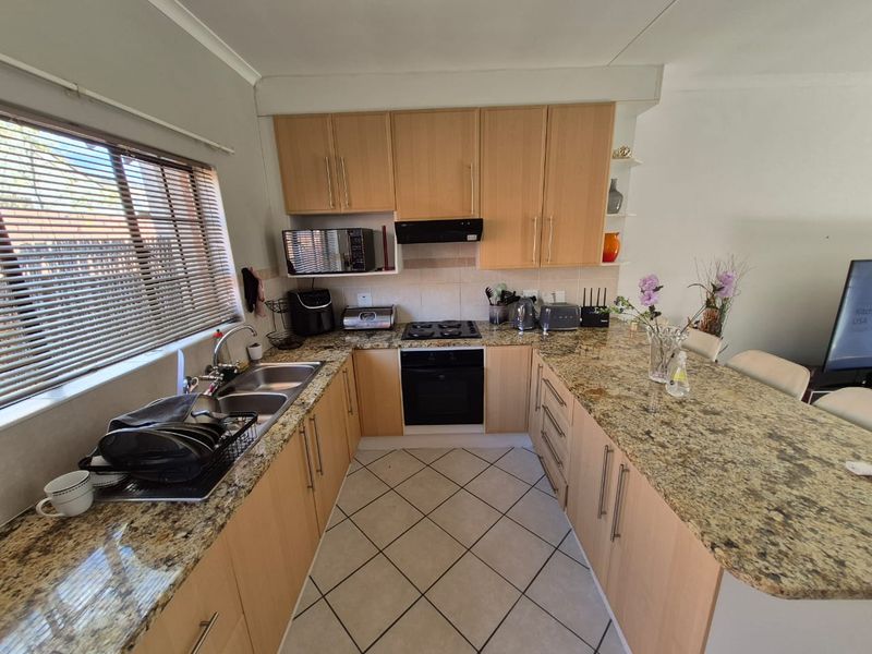 A functional kitchen featuring granite countertops, light wood cabinetry, a built-in oven with gas hob, and tiled flooring with a breakfast bar area.