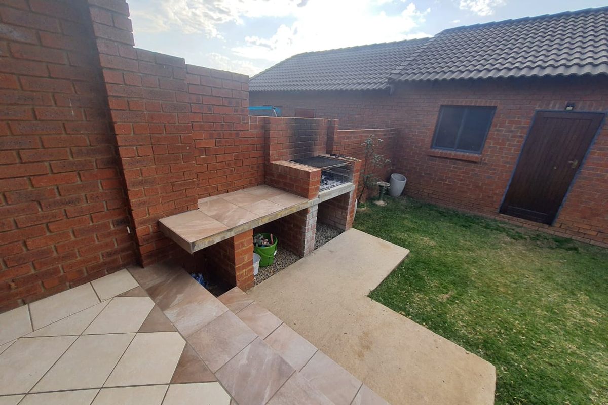 Rear garden area featuring a built-in brick braai, tiled patio space, and direct access to the main dwelling structure.