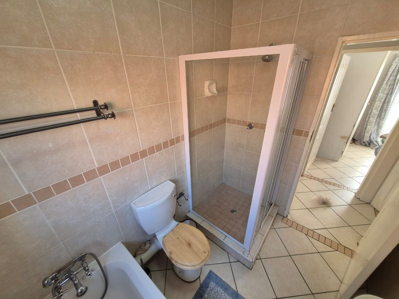 A functional bathroom featuring a shower enclosure, bathtub, and toilet with neutral wall and floor tiling.