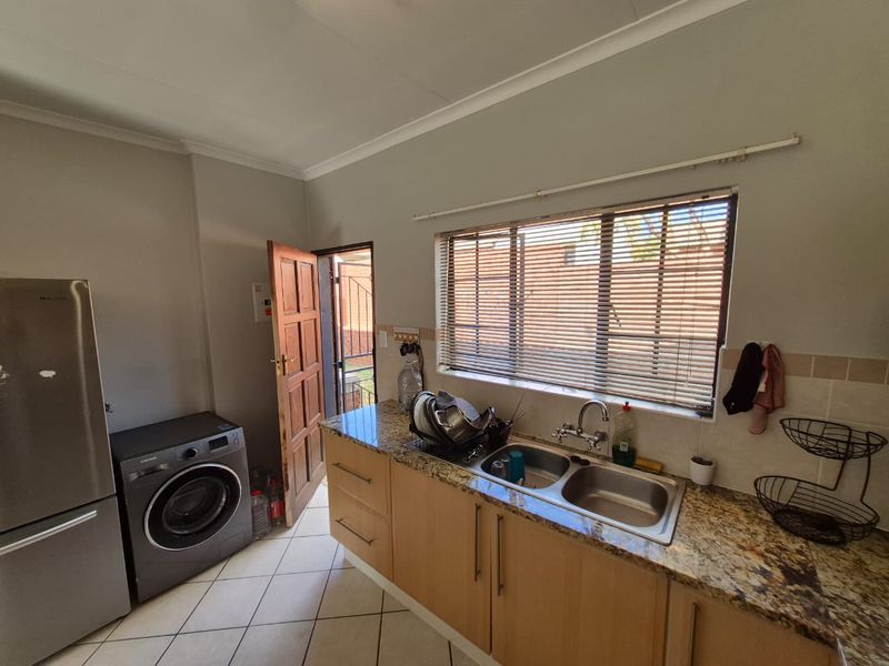 A functional kitchen featuring granite countertops, wooden cabinetry, double bowl stainless steel sink, and tiled flooring with direct access to the exterior.
