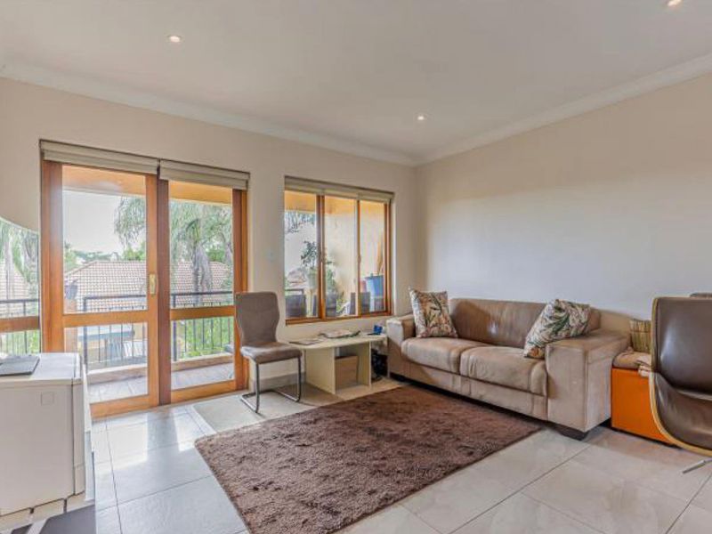 A bright living room featuring tiled flooring, recessed downlights, and sliding glass doors that provide direct access to an outdoor balcony area.