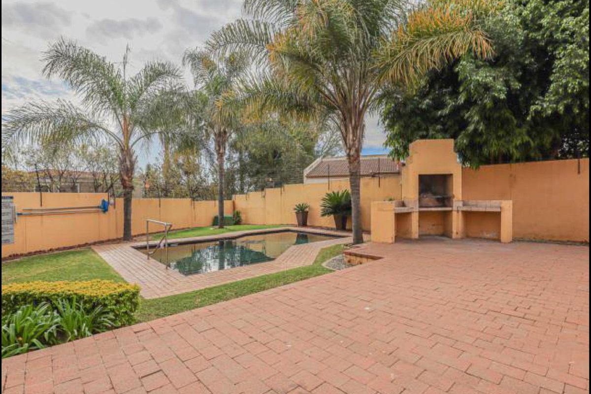 Outdoor entertainment area featuring a swimming pool, paved patio, and a built-in brick braai, enclosed by a perimeter wall.