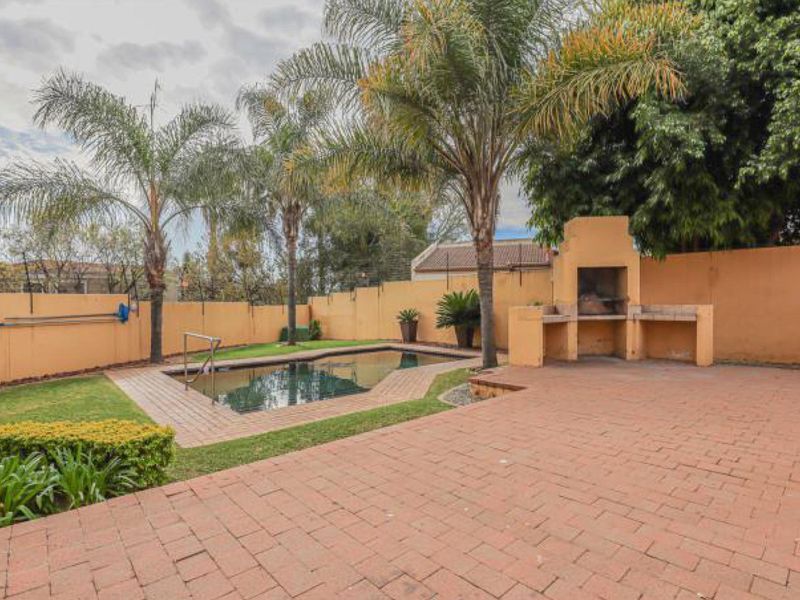 Outdoor entertainment area featuring a swimming pool, paved patio, and a built-in brick braai, enclosed by a perimeter wall.
