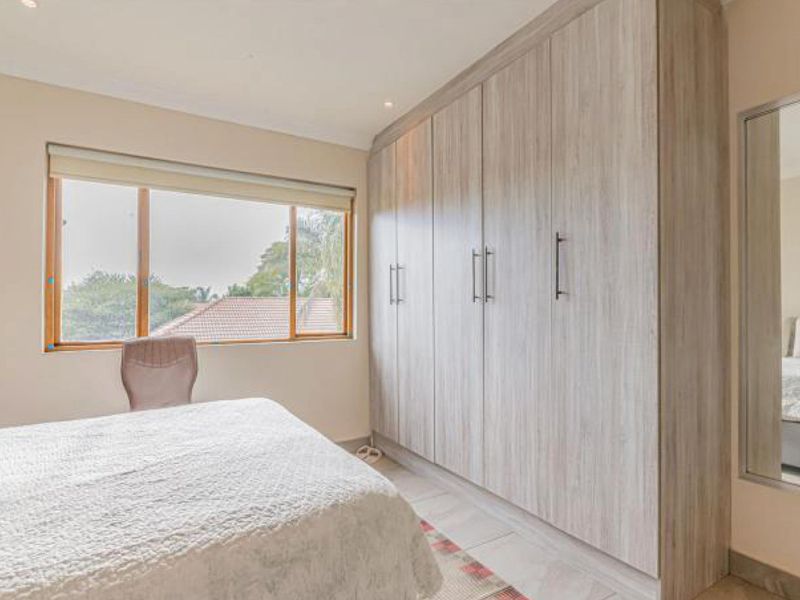 A well-maintained bedroom featuring extensive built-in cupboards, tiled flooring, and a large window providing natural light and exterior views.