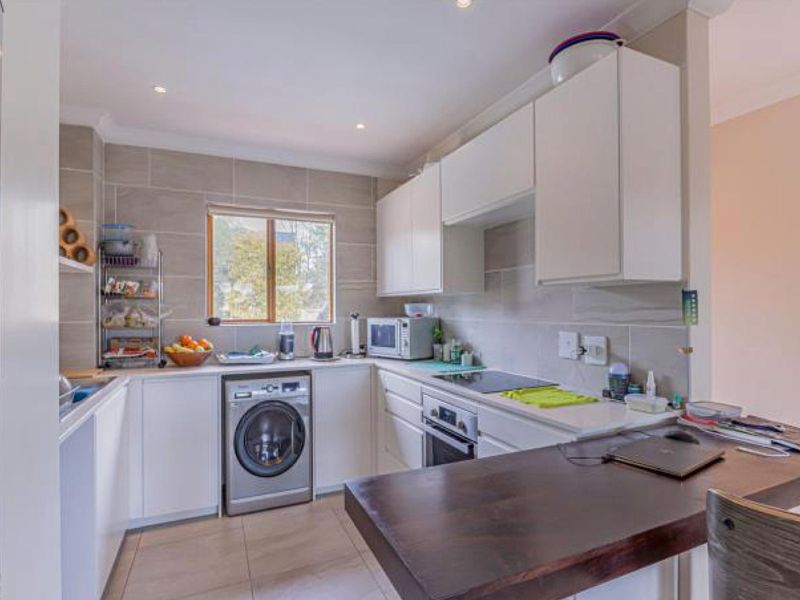 A functional kitchen featuring white cabinetry, stone countertops, a breakfast bar, and integrated appliances with neutral tiled finishes.