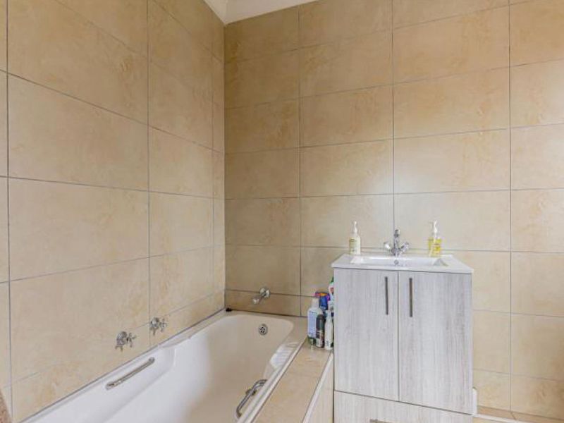 A functional bathroom featuring a built-in bathtub and a modern vanity cabinet with a washbasin, finished with neutral wall tiling.