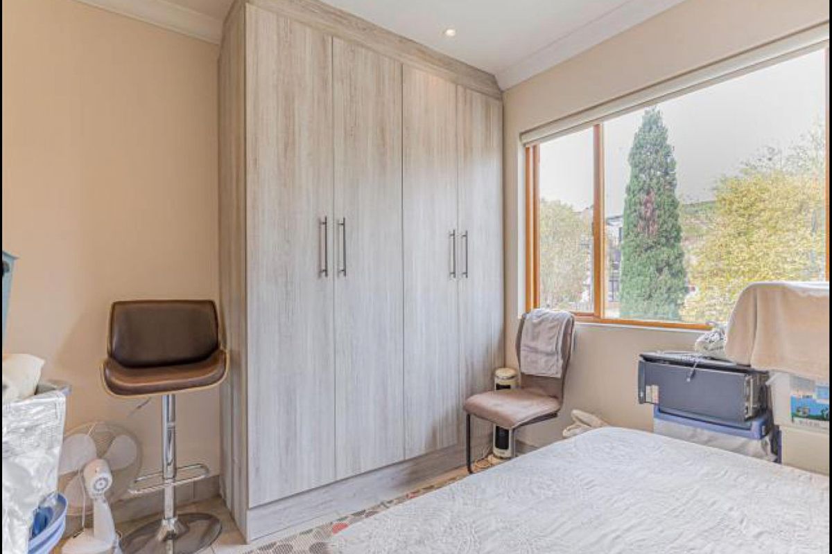 A bedroom featuring light wood-grain built-in wardrobes, a large window providing natural light, and recessed ceiling lighting.