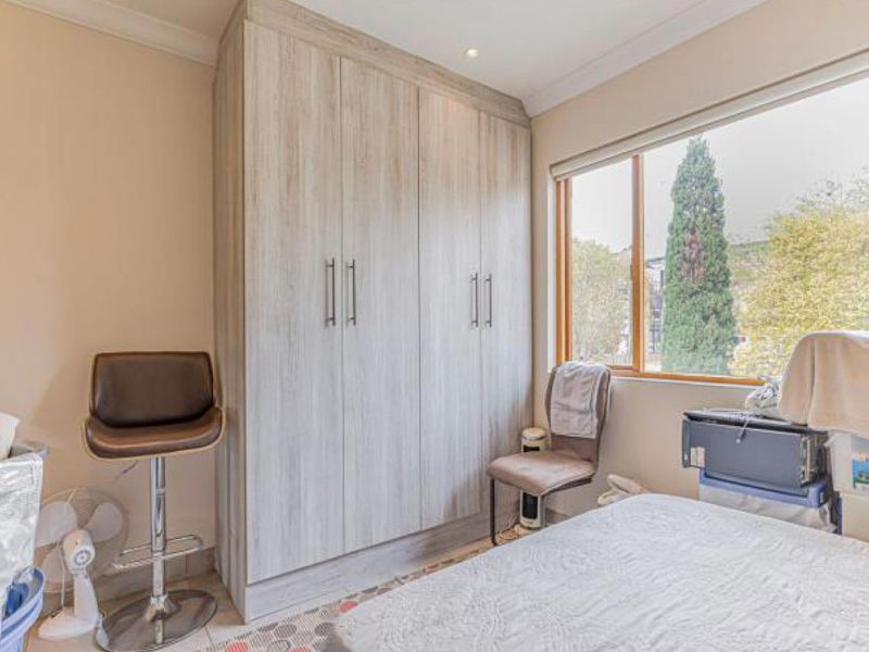 A bedroom featuring light wood-grain built-in wardrobes, a large window providing natural light, and recessed ceiling lighting.