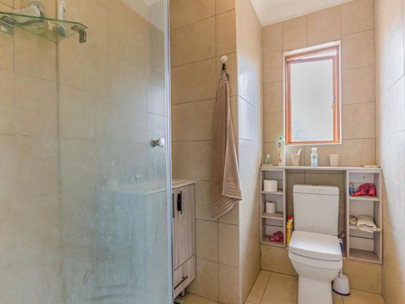 A functional bathroom featuring a glass-enclosed shower, built-in shelving, and neutral ceramic tiling throughout.